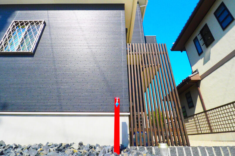 ネイビーの建物に映えるポストと同じ差色の赤い立水栓。